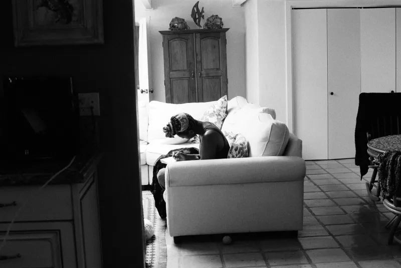 A person curled up asleep on a sofa in a bright living room, in black and white