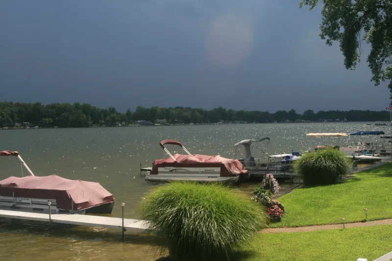 Pontoon boats moored on a lake under a dark sky, green lawn in front