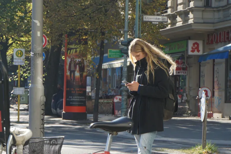 A young woman with long blond hair looking at her phone on a sunny city street corner