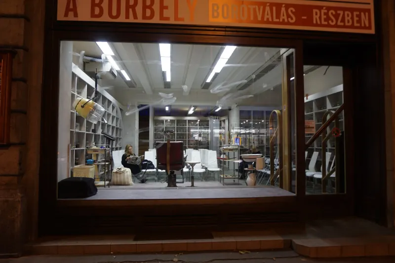 A lit shop window at night, seen from the dark street, a person sitting inside