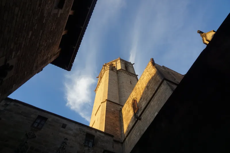 A sandstone church tower against a blue sky, seen from below between dark walls