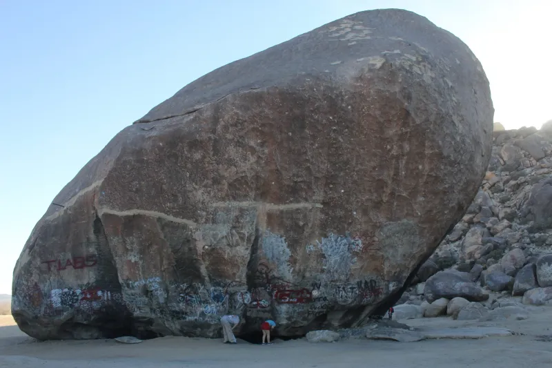 An enormous boulder covered in graffiti, a small figure at its base