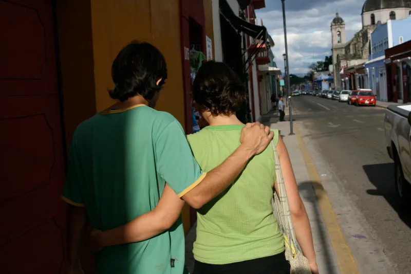 Two boys walking down a sunny street with their arms around each other