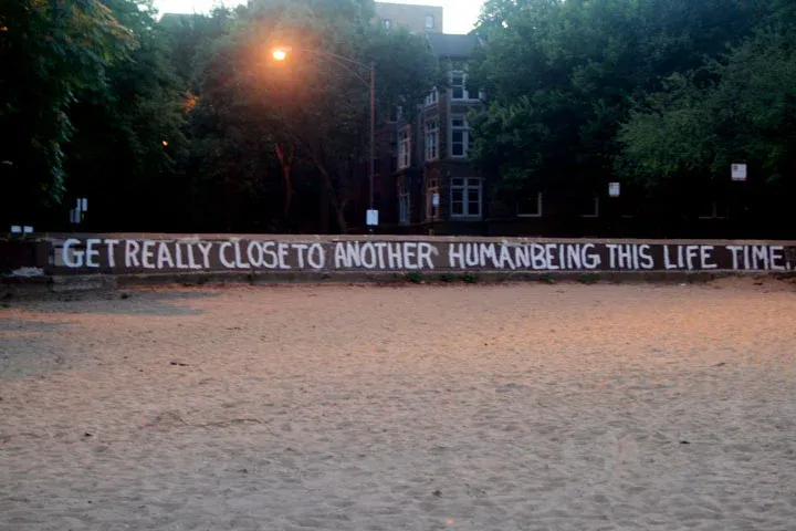 Words painted on a low wall at dusk: "Get really close to another human being this life time"