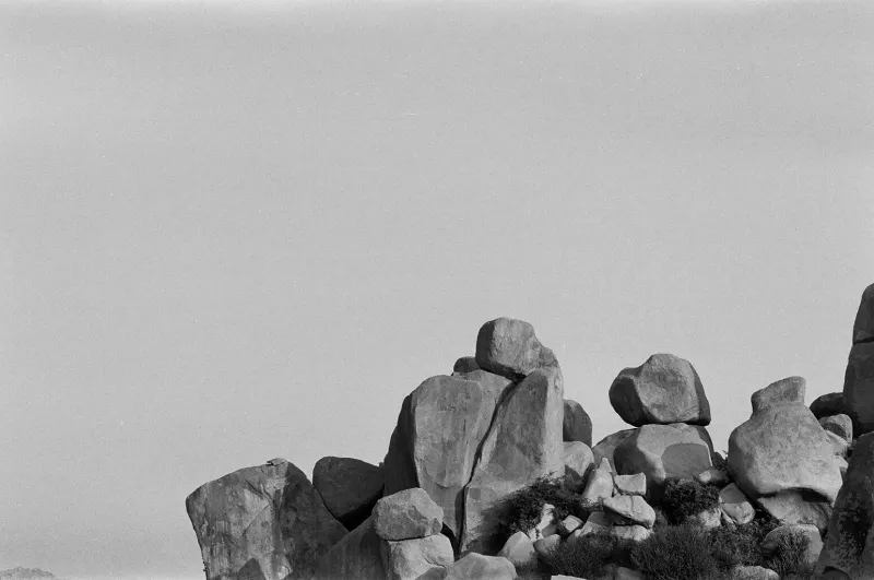 A pile of large boulders under a pale sky, in black and white