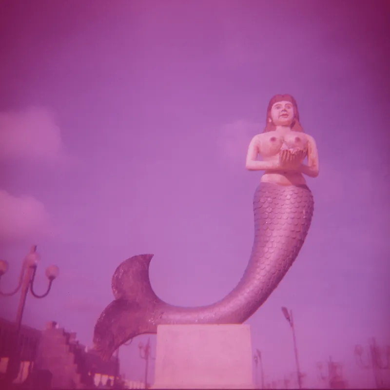 A statue of a mermaid against a pink sky
