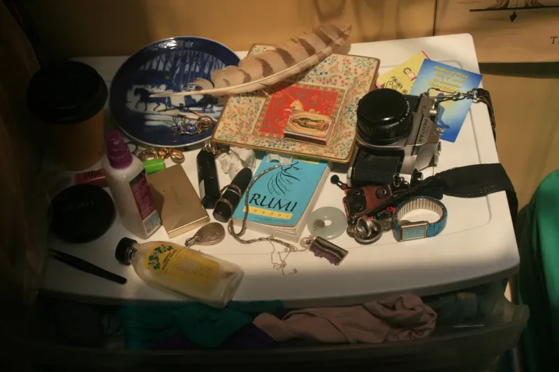A cluttered dressing table with a camera, a feather, a Rumi book and small keepsakes