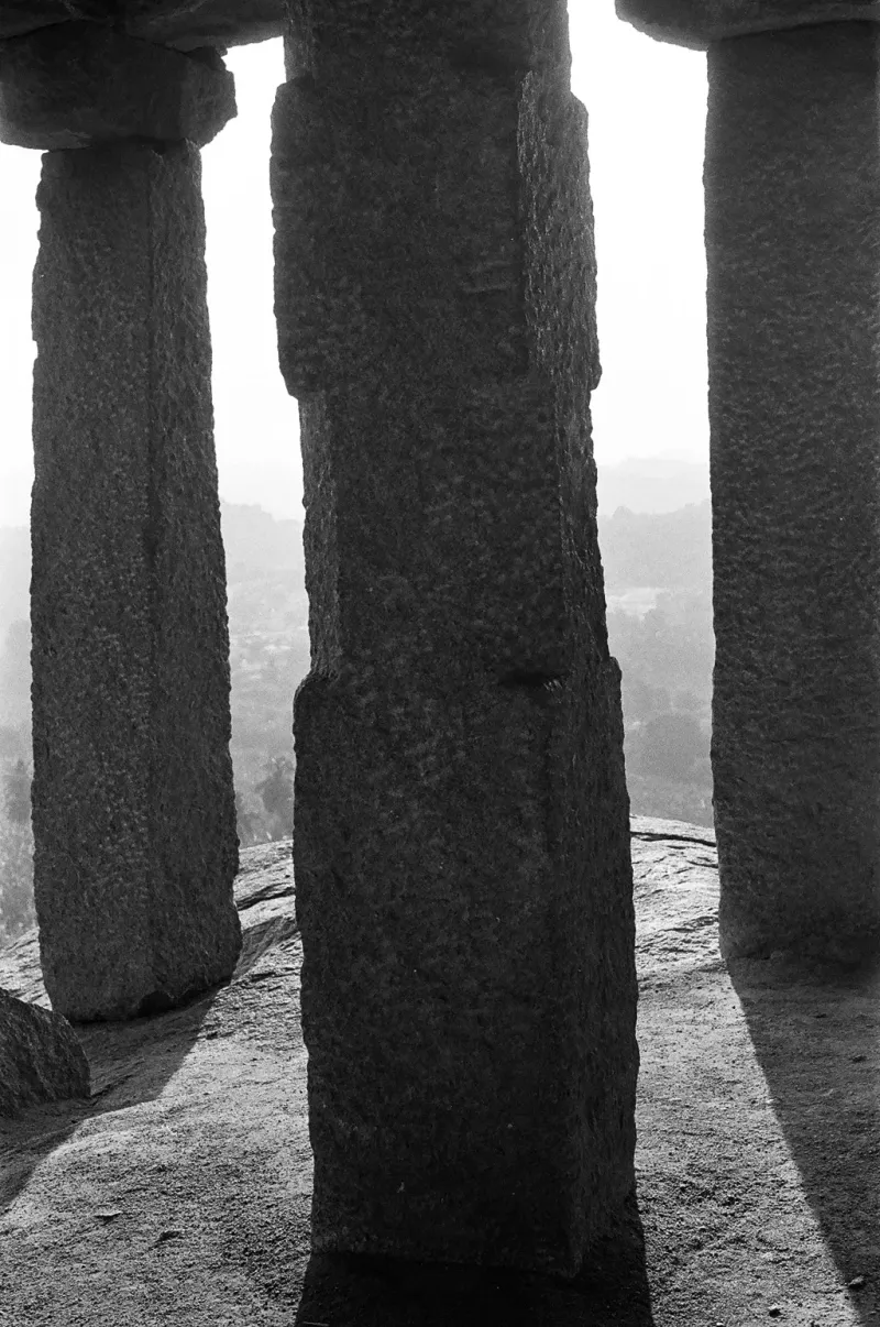 Stone pillars of an old temple, a hazy view between them, in black and white